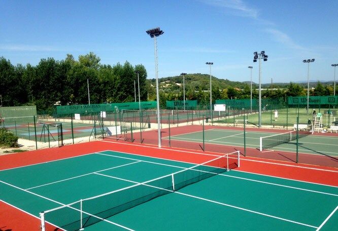 The village tennis courts at Sommières, green and red hard courts under floodlights with wooded hills behind